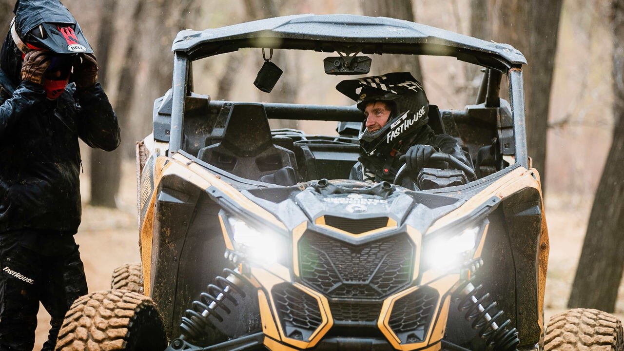 A Can-Am unit with a driver talking to a man outside of the unit, both with helmets on
